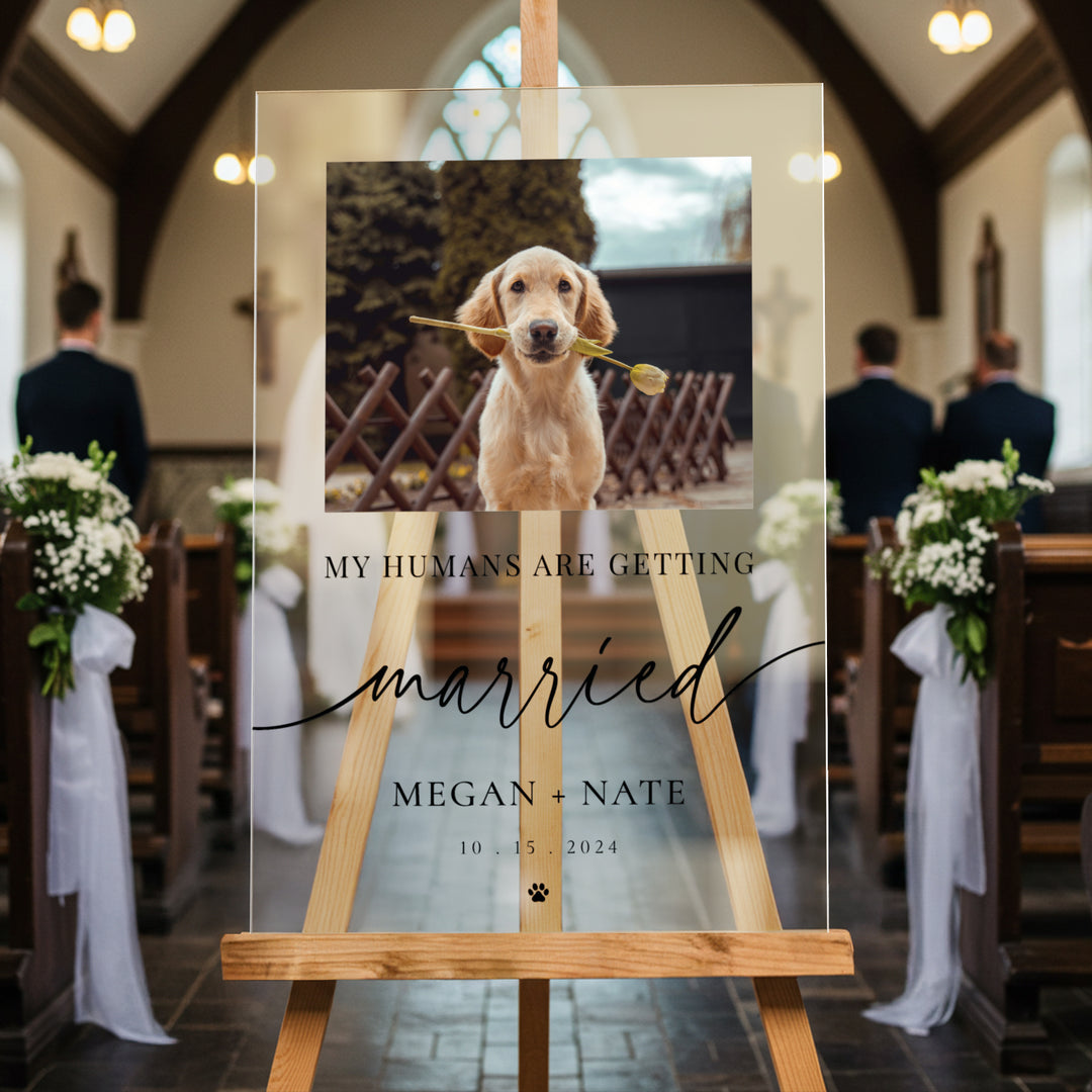 Acrylic wedding sign with a puppy holding a flower, placed on an easel in a church setting.