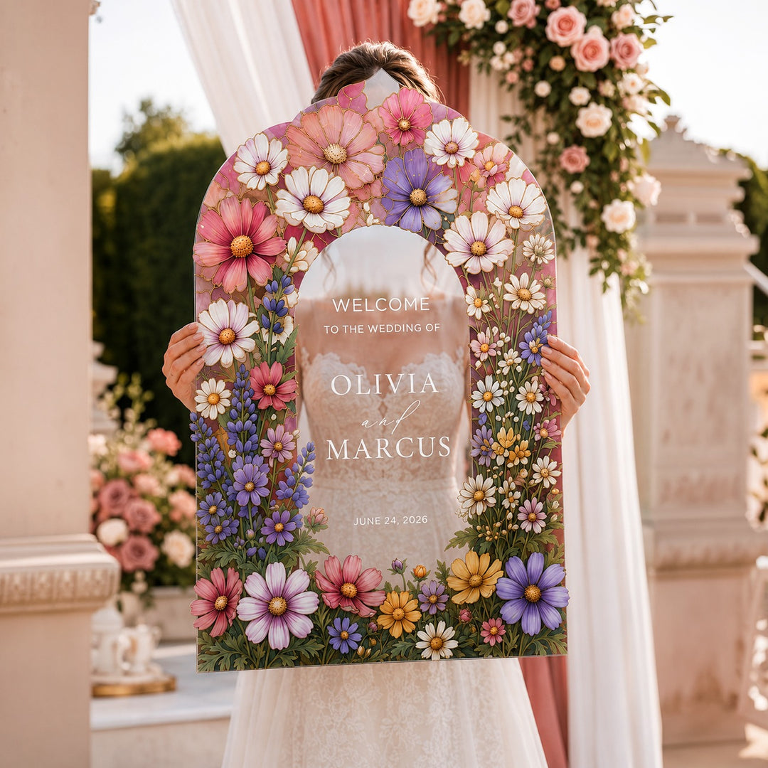 Floral welcome sign for a wedding held by a person in an elegant outdoor setting. Enchanted Garden Pink Cosmos Wedding Welcome Sign. Clear acrylic wedding custom sign.