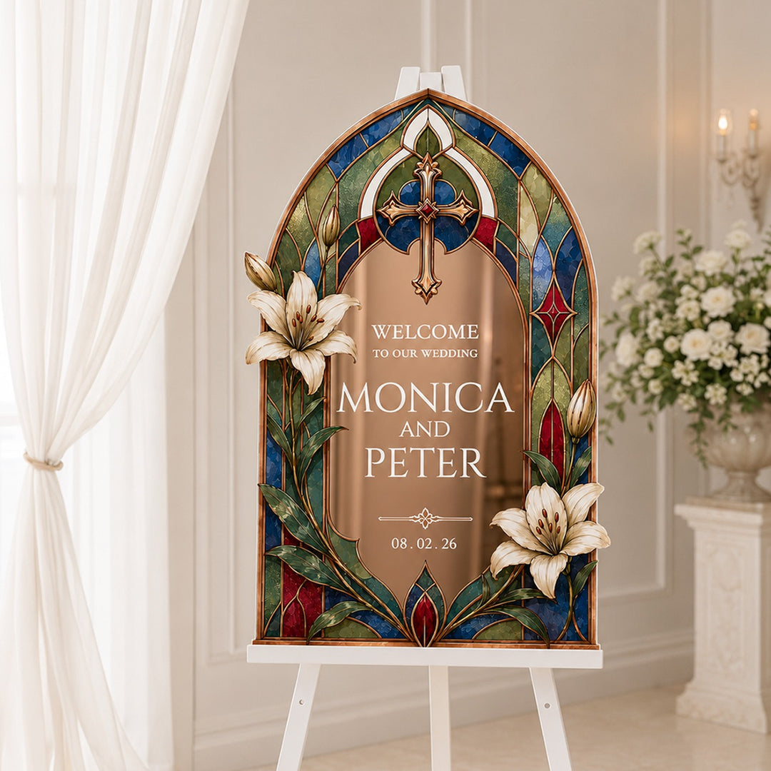 A personalized stained-glass-style wedding sign on a white easel in a softly lit indoor setting. The sign has an arched Gothic window design with blue, green, red, and gold stained-glass panels, white lily flowers, and a central gold panel with custom text. Gothic Cathedral Lily Stained Glass Wedding Welcome Sign, Rose Gold mirror acrylic.