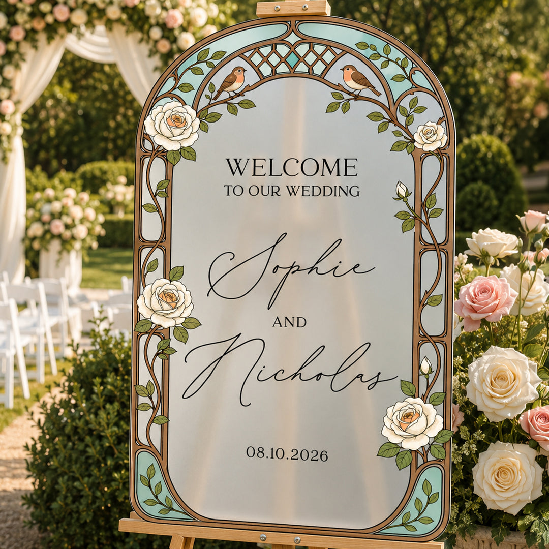 Teal stained glass cream rose wedding welcome sign on easel at outdoor reception with couple.