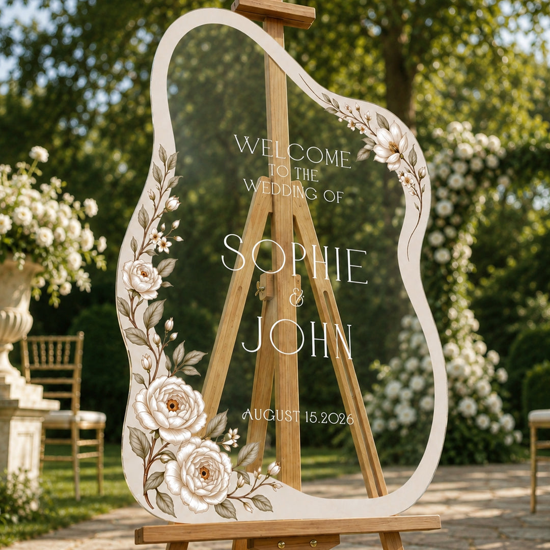 Cream peony wavy shape wedding welcome sign on easel at summer outdoor ceremony.